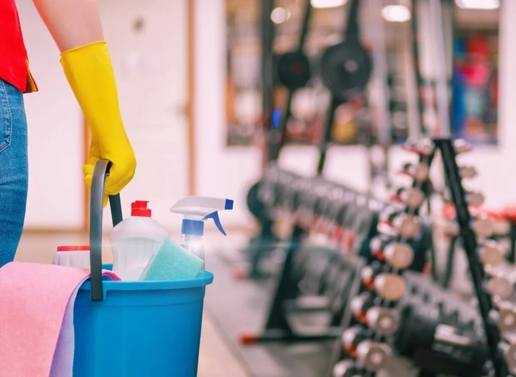 A person carrying a bucket of household cleaning supplies.